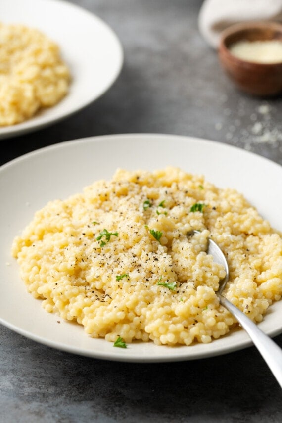 Pastina is served on a white plate topped with black pepper and parmesan cheese.