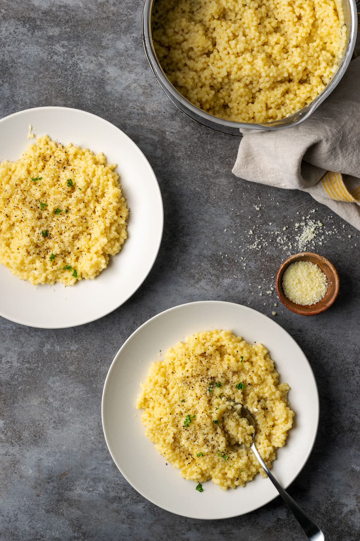 Two servings of pastina on white plates next to a pan of pastina pasta.