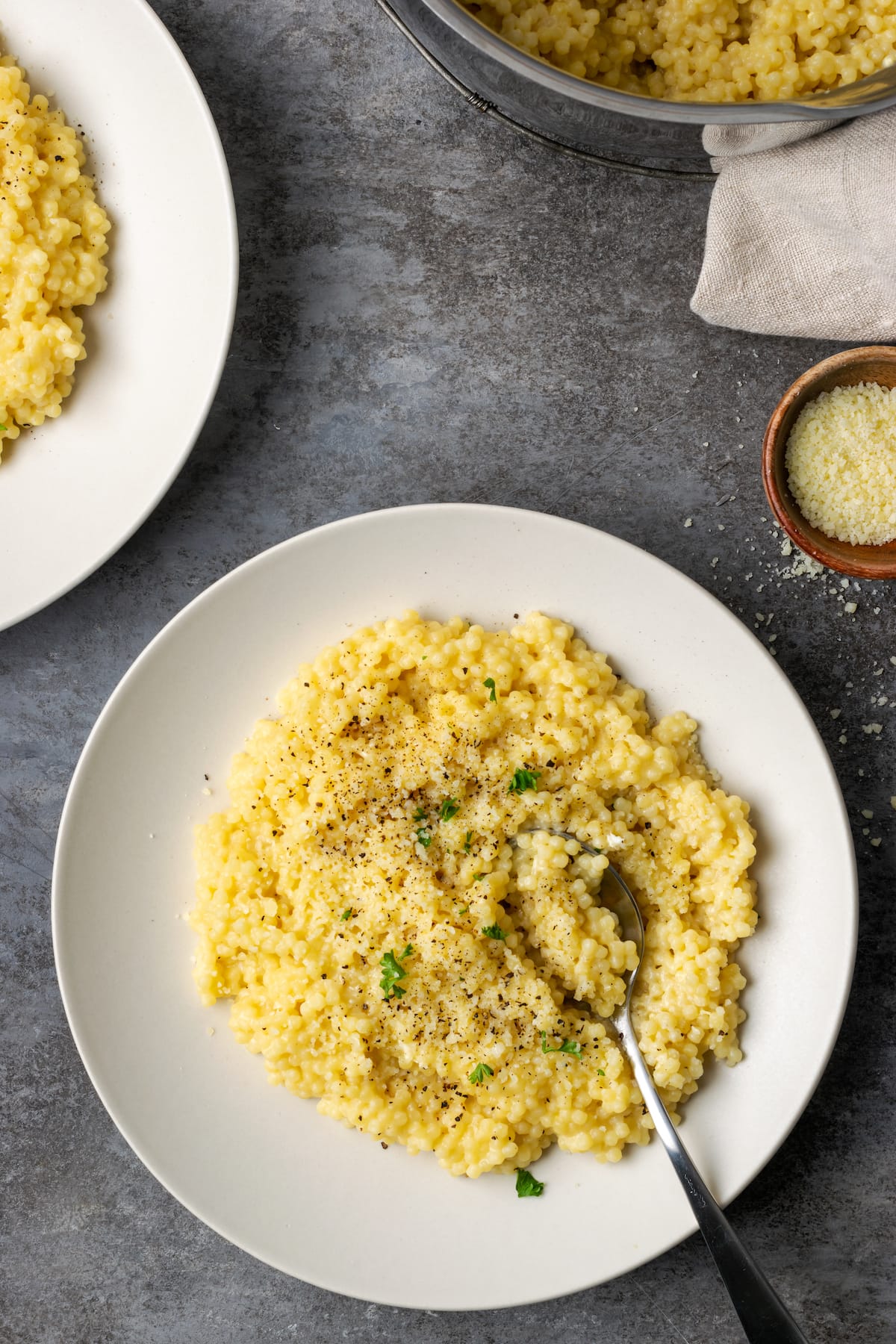 Vue aérienne de la pastina servie sur une assiette blanche garnie de poivre noir et de parmesan.