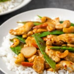 Cashew chicken served over a bed of jasmine rice on a plate.
