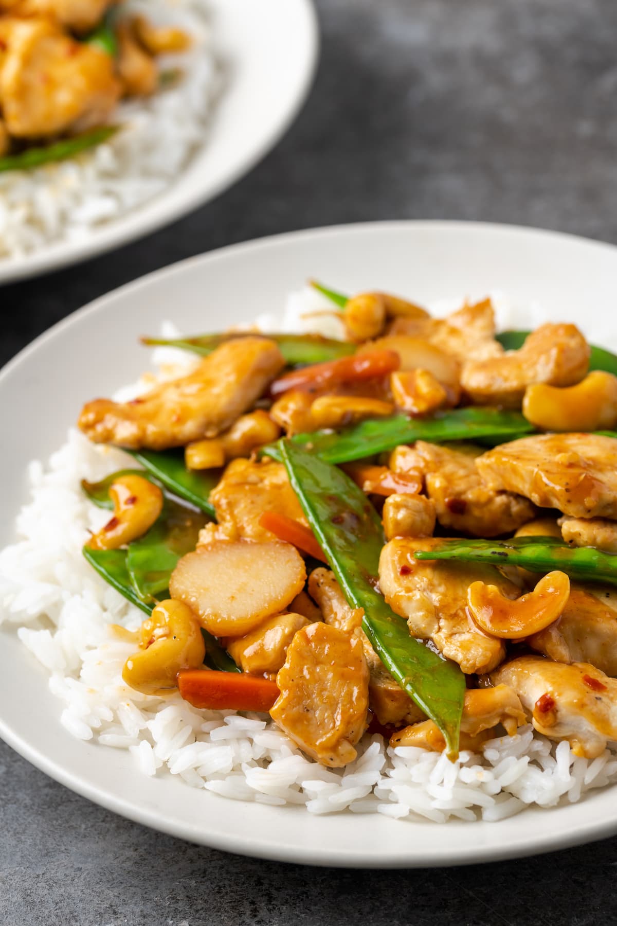 Cashew chicken served over a bed of jasmine rice on a plate.