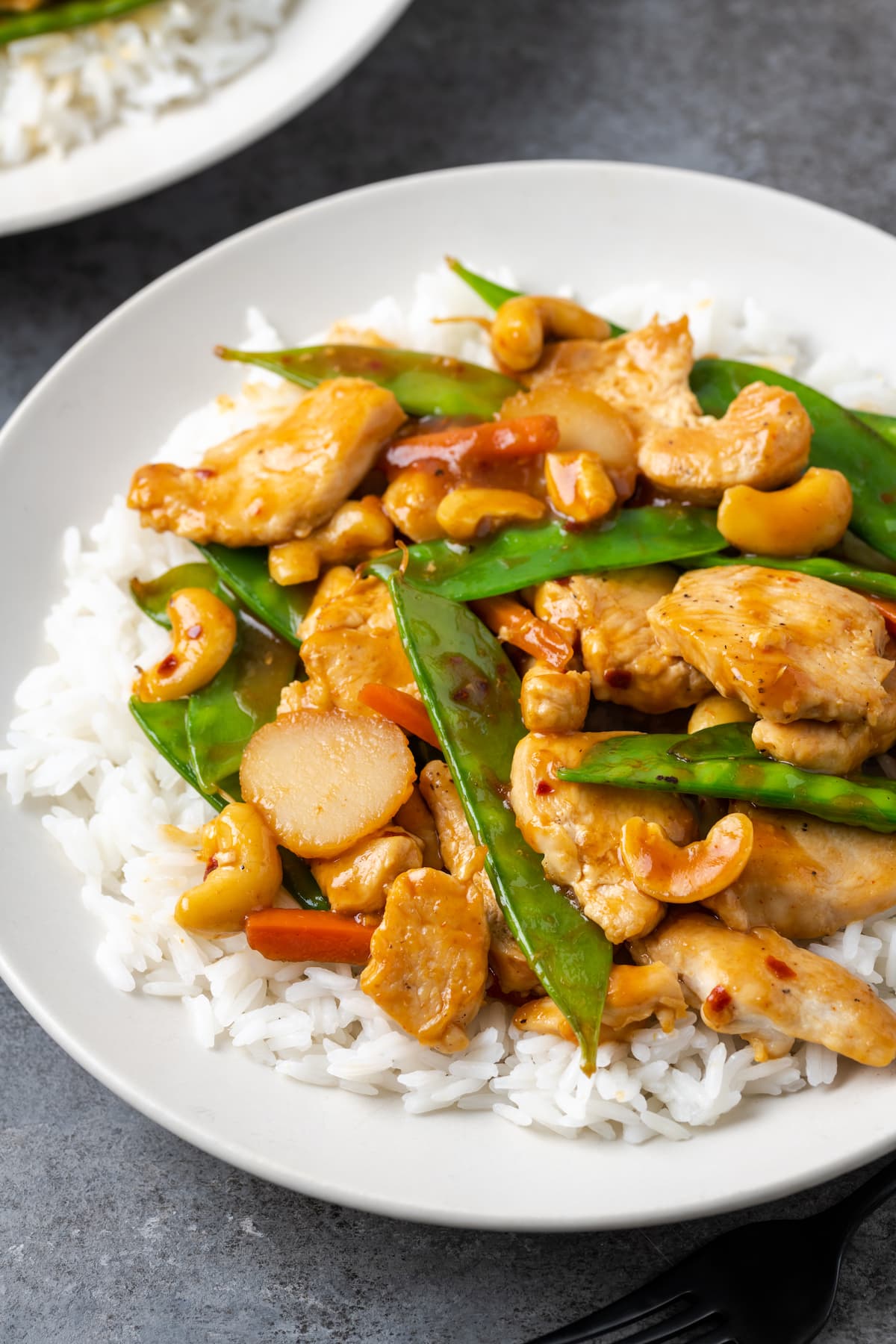 Cashew chicken served over a bed of jasmine rice on a plate.