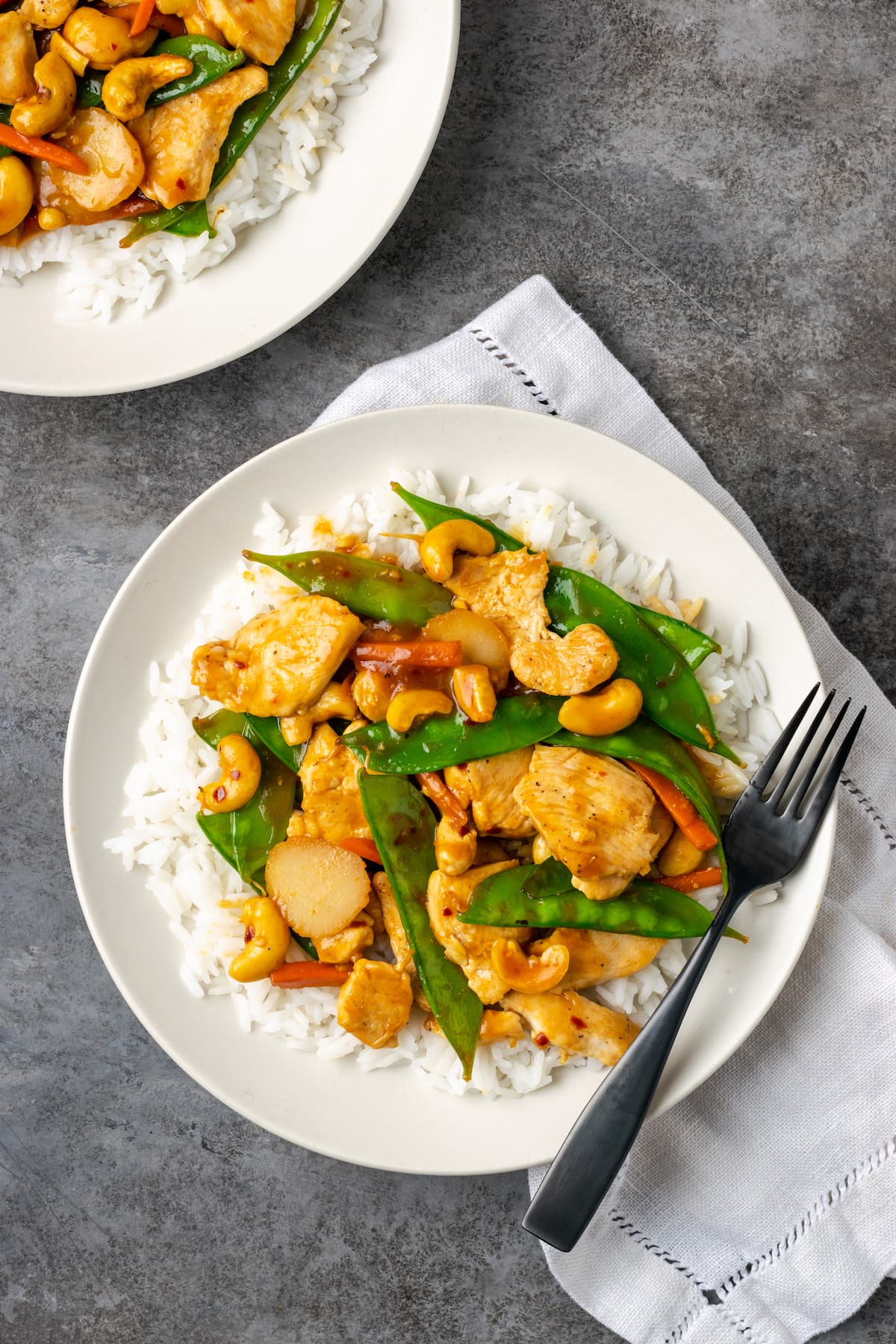 Overhead view of cashew chicken served over a bed of jasmine rice on a plate, next to a fork.