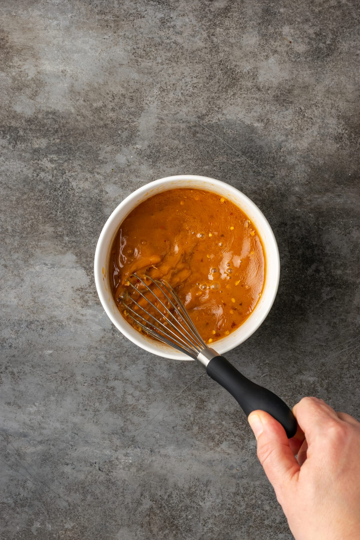 A hand using a whisk to combine the stir fry sauce ingredients for cashew chicken.