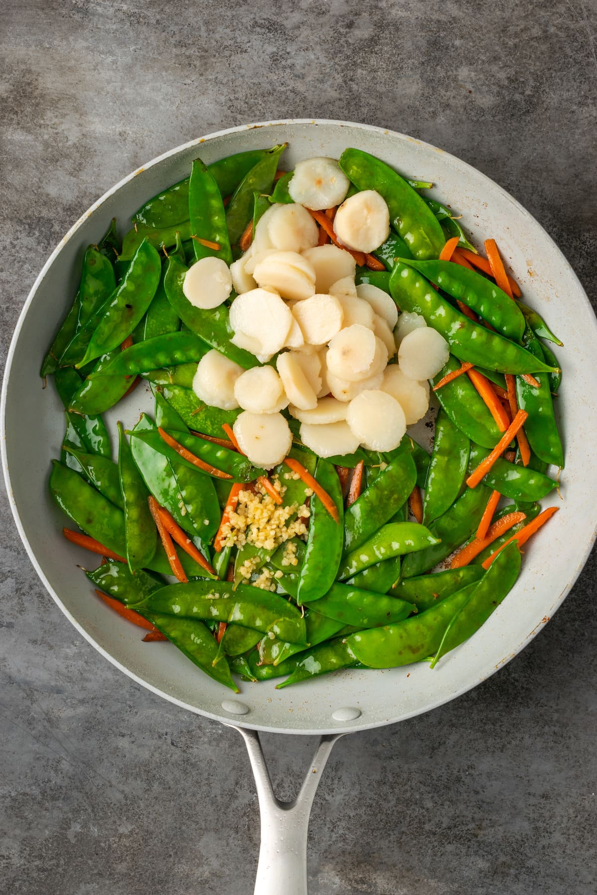 Water chestnuts added to a skillet with sautéd snow peas and carrots.