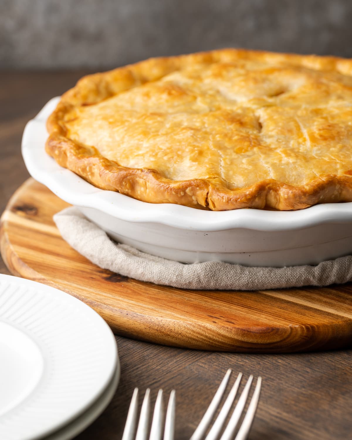 Baked chicken pot pie inside a pie plate next to stacked white plates and two forks.
