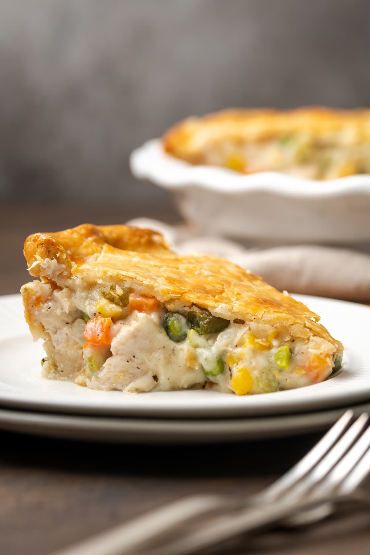 A slice of chicken pot pie on a white plate next to a fork.