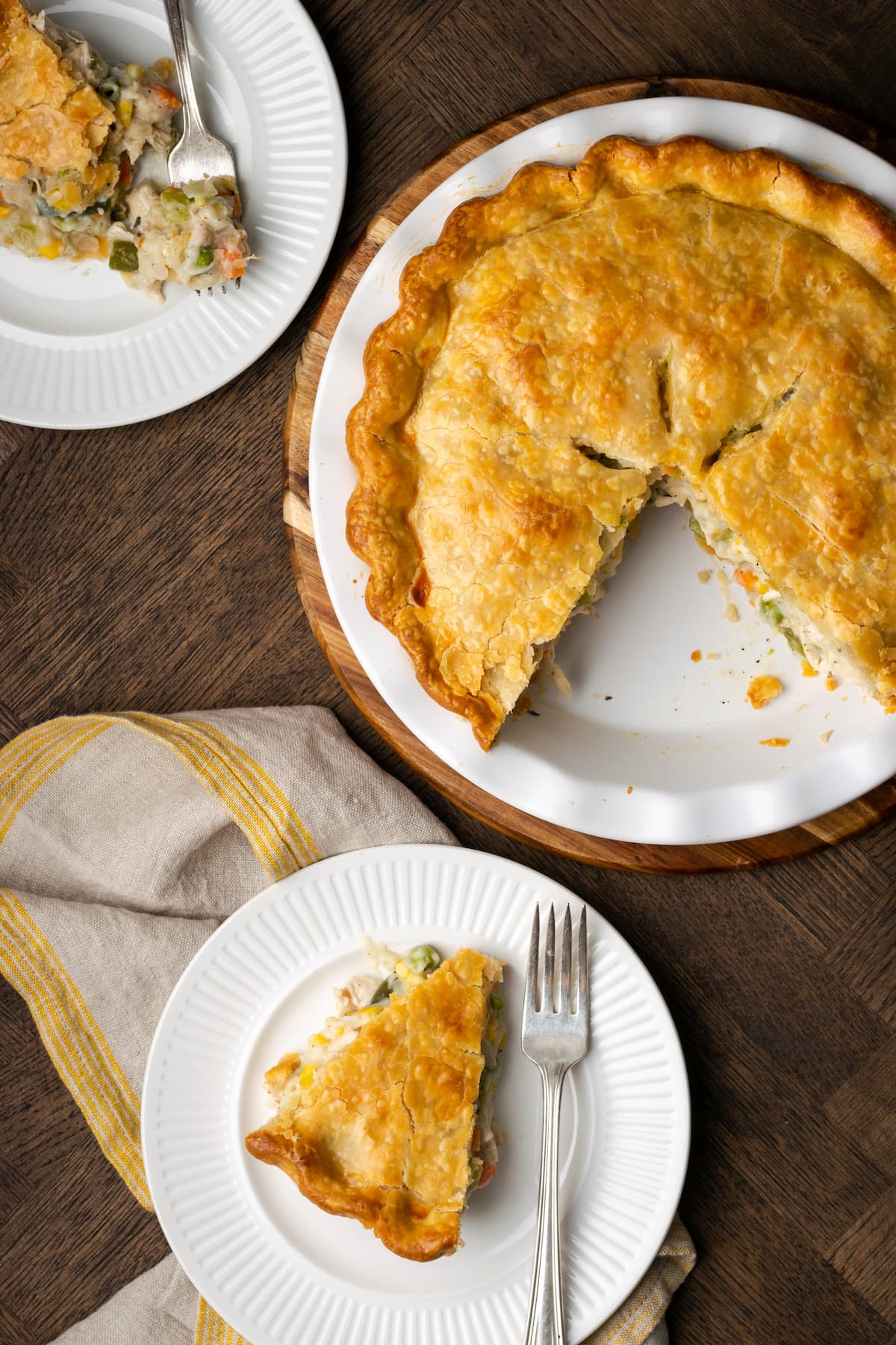 Overhead view of a chicken pot pie with slices missing, served on two nearby plates.