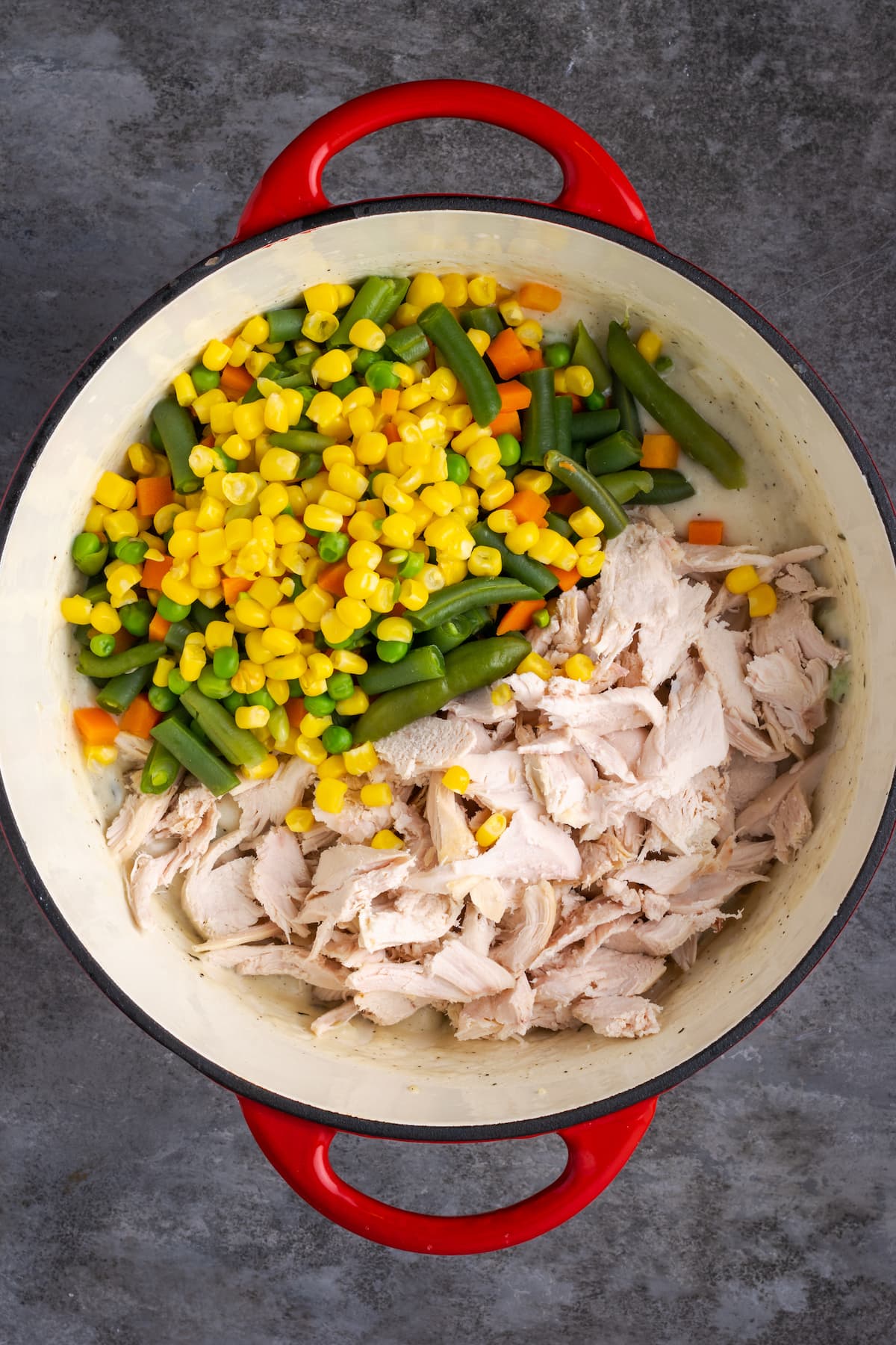 Shredded chicken and cooked frozen veggies added to the chicken pot pie cream sauce in a pot.