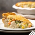 A slice of chicken pot pie on a white plate next to a fork.