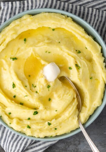A spoon stuck into a bowl of creamy Instant Pot mashed potatoes topped with butter.