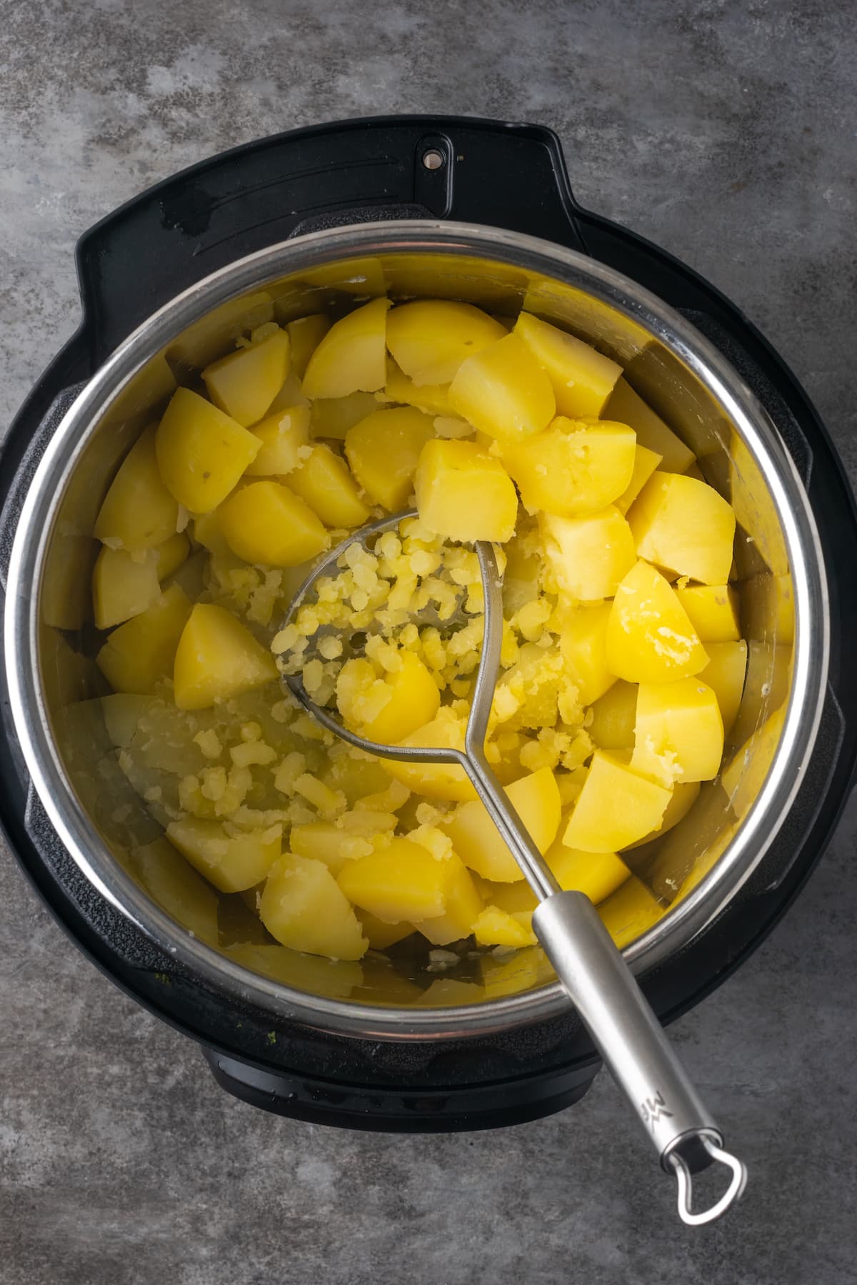 A potato masher is used to mash cooked chopped potatoes inside an Instant Pot.