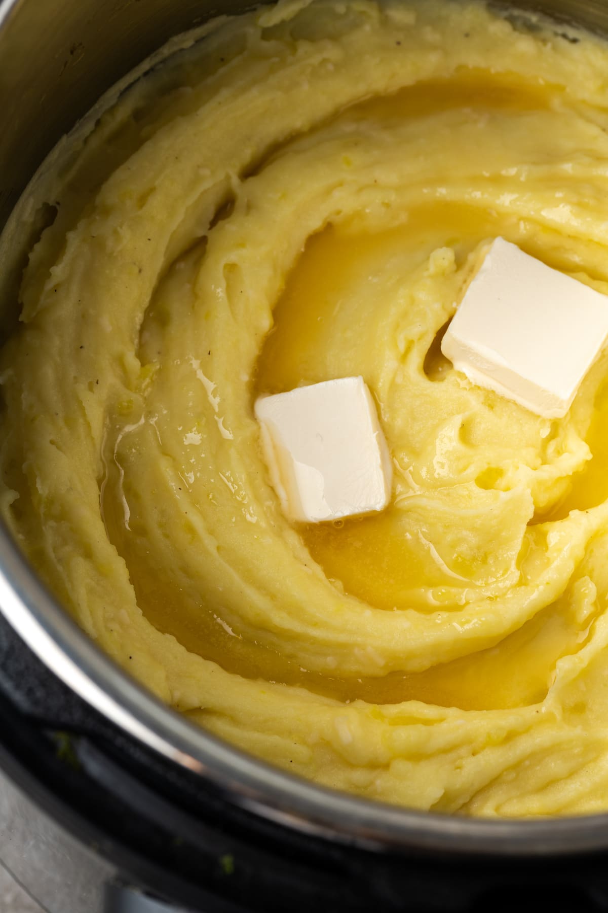 Two pats of butter added to creamy mashed potatoes inside the Instant Pot.