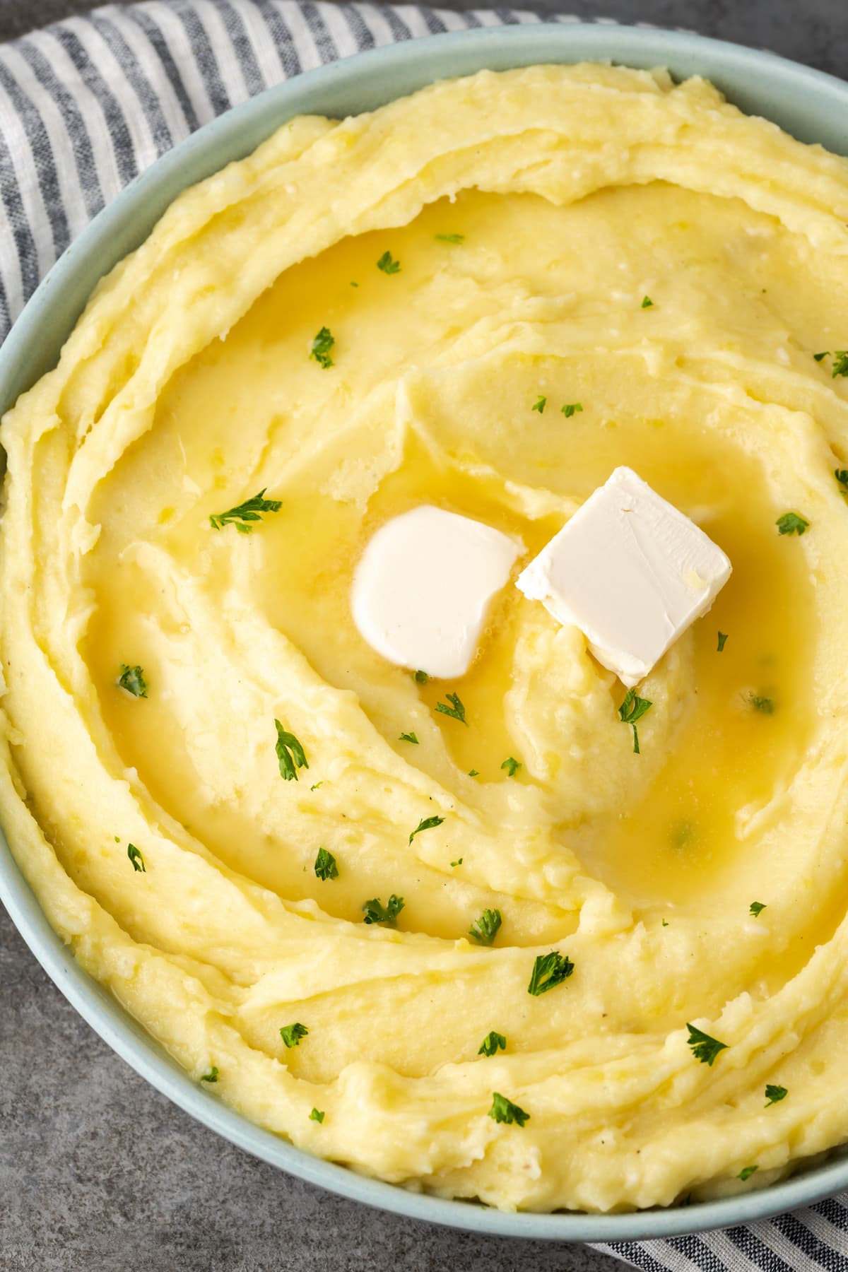 Creamy Instant Pot mashed potatoes in a bowl topped with two pats of butter and chives.