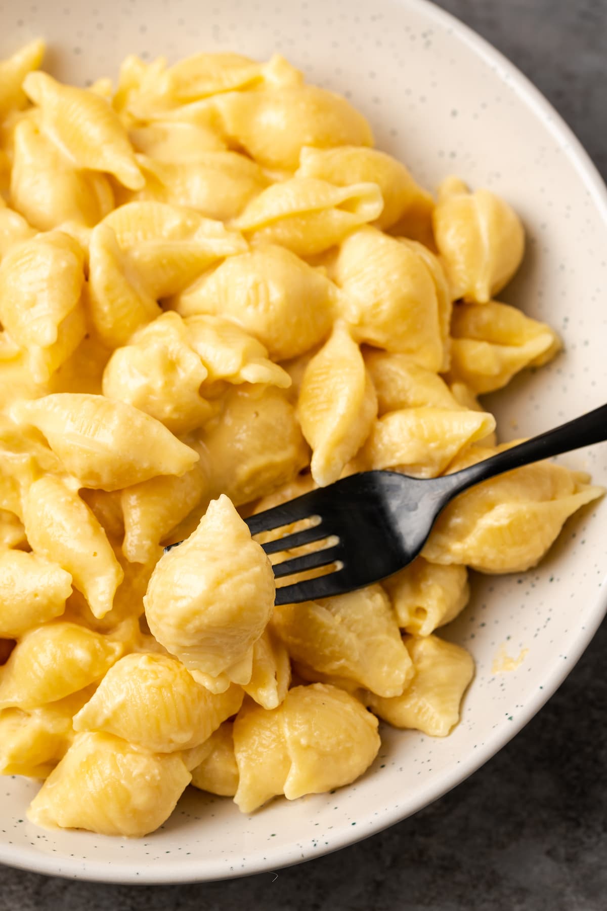 A fork picking up a bite from a bowlful of mac and cheese.