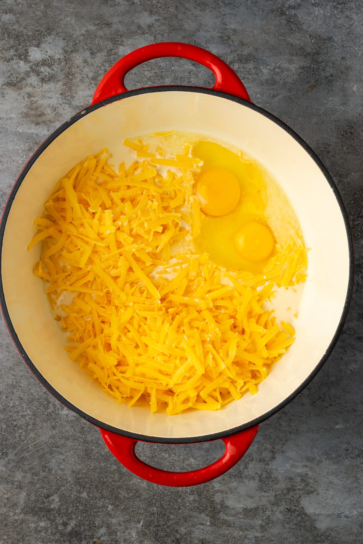 Grated cheddar cheese, eggs, and sauce ingredients combined in a large pot.