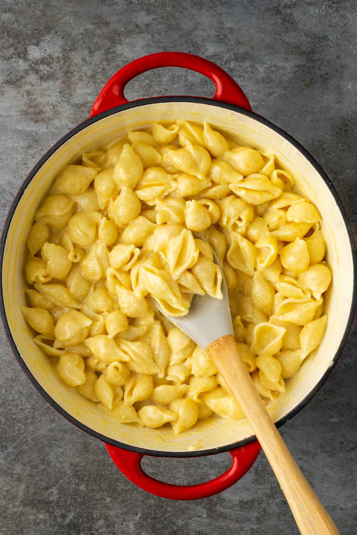 Shell pasta coated in cheese sauce in a large pot with a stirring spoon.