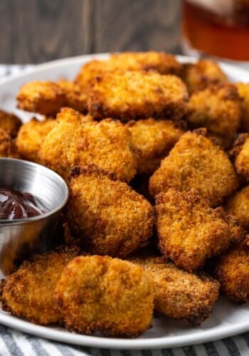 Crispy air fryer popcorn chicken on a white place next to a ramekin of BBQ sauce for dipping.