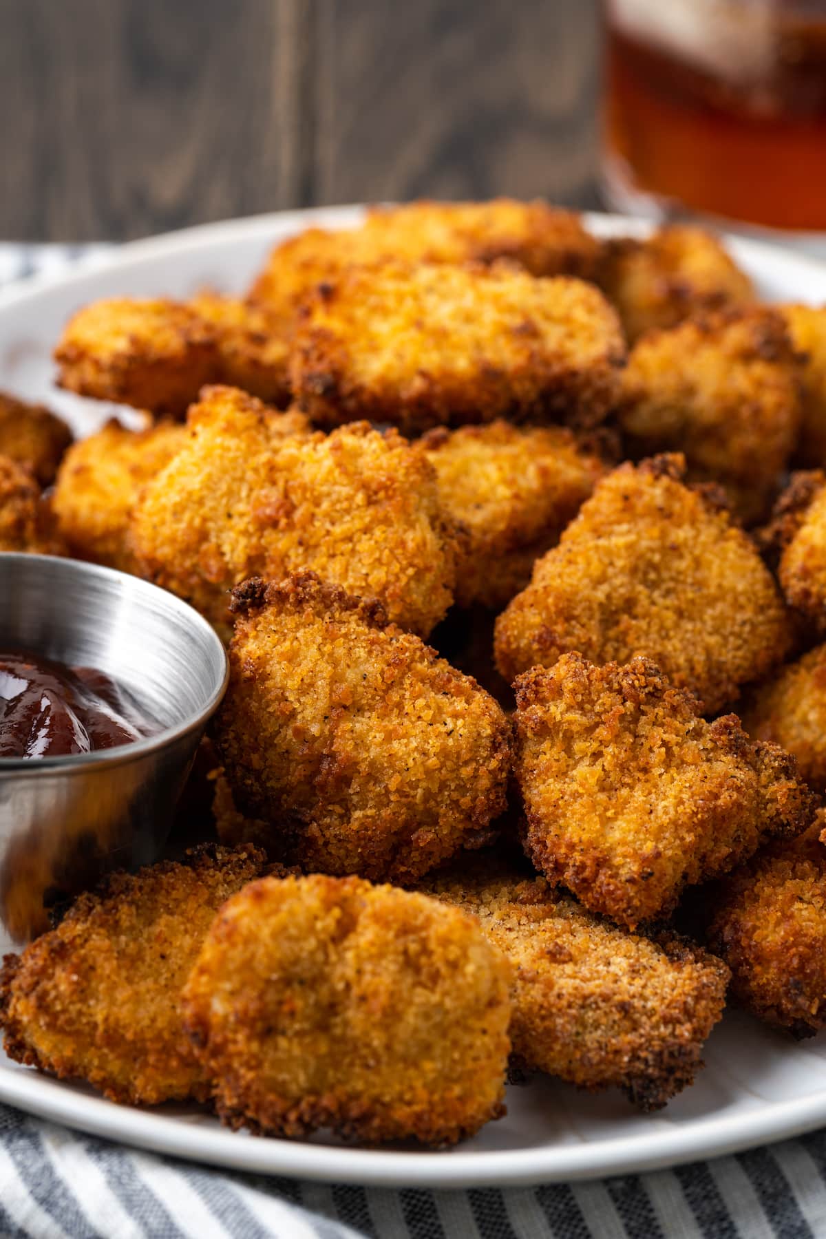 Crispy air fryer popcorn chicken on a white place next to a ramekin of BBQ sauce for dipping.