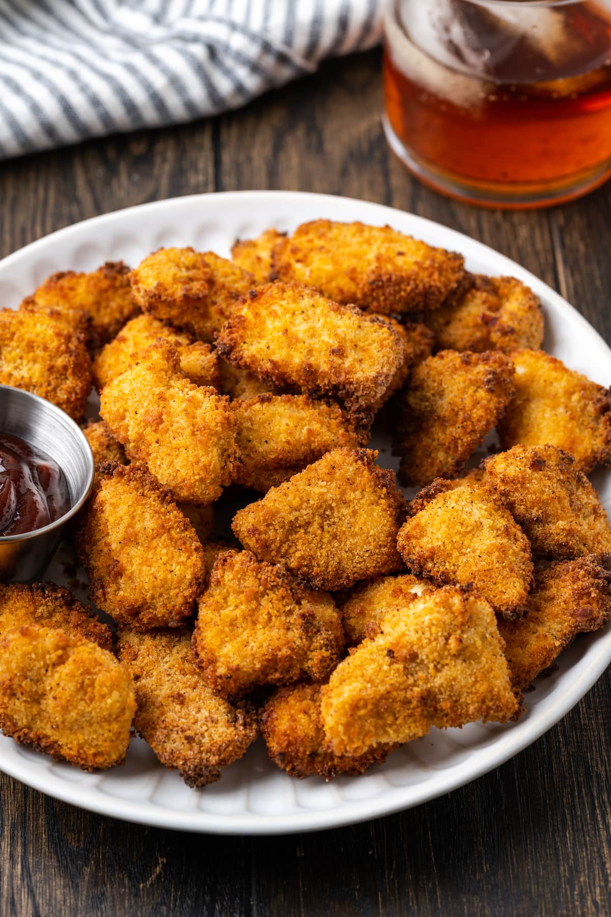 Crispy air fryer popcorn chicken on a white place next to a ramekin of BBQ sauce for dipping.