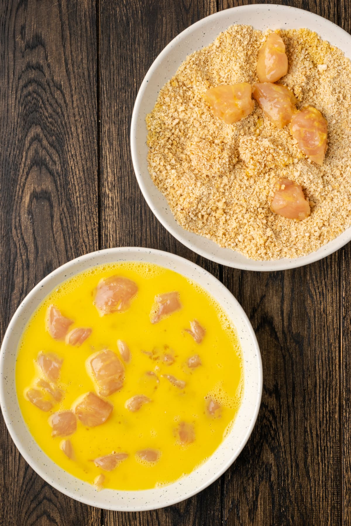 Chicken pieces in an egg wash next to another dish with chicken being coated in breadcrumbs.