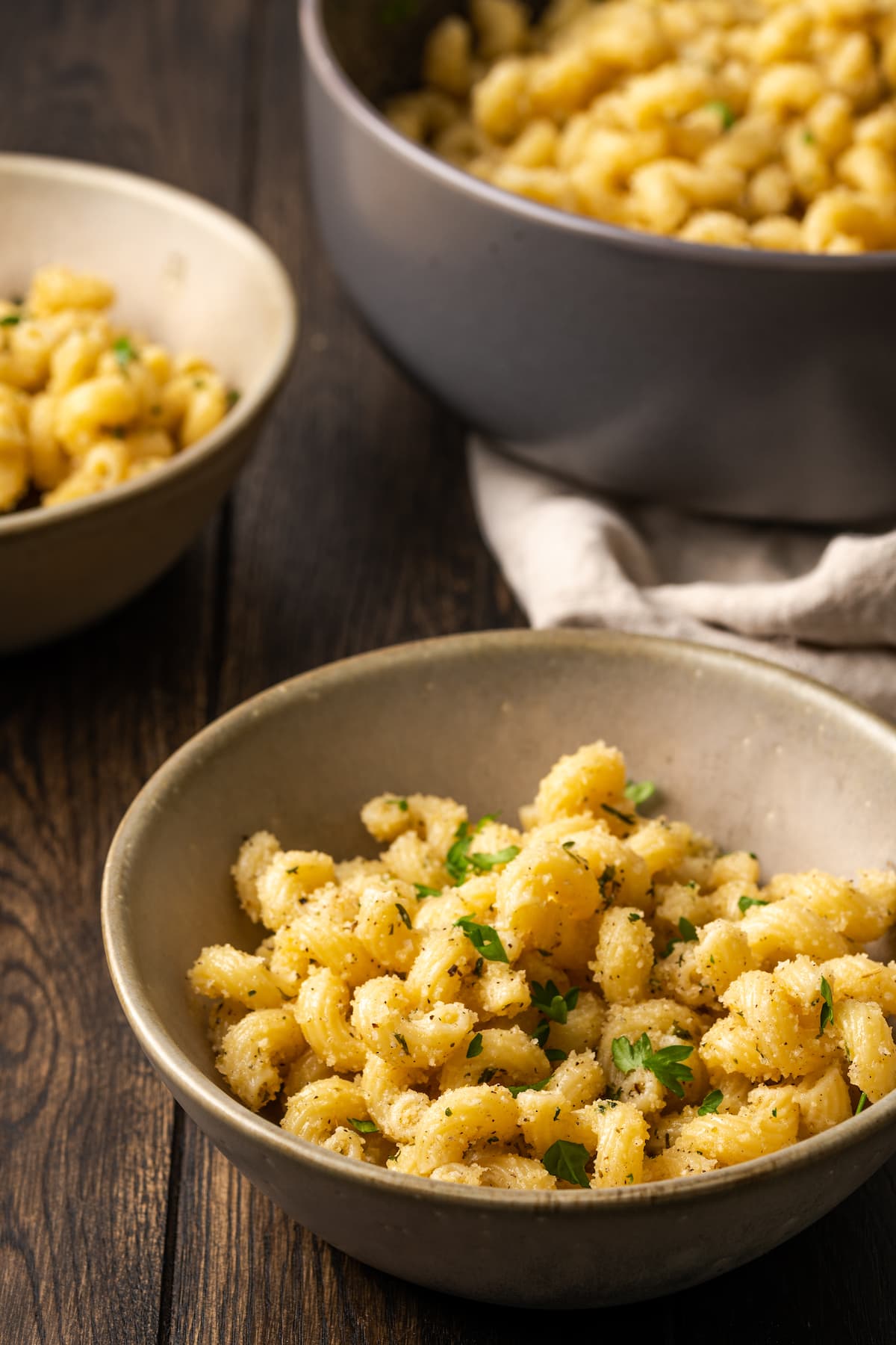 A bowl of garlic bread pasta with a second bowl and a pot of pasta in the background.