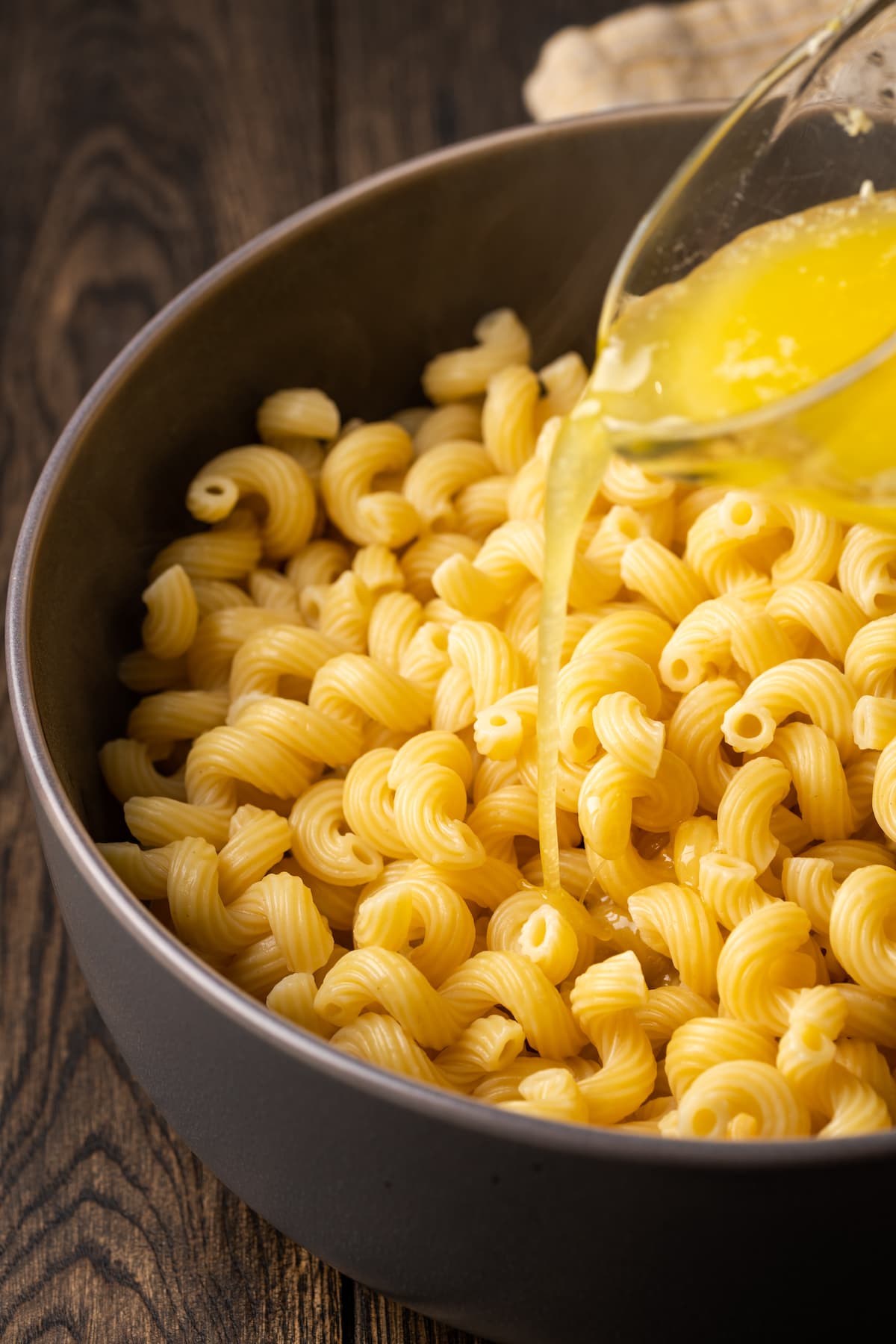 Melted garlic butter is poured over top of cooked pasta in a large pot.