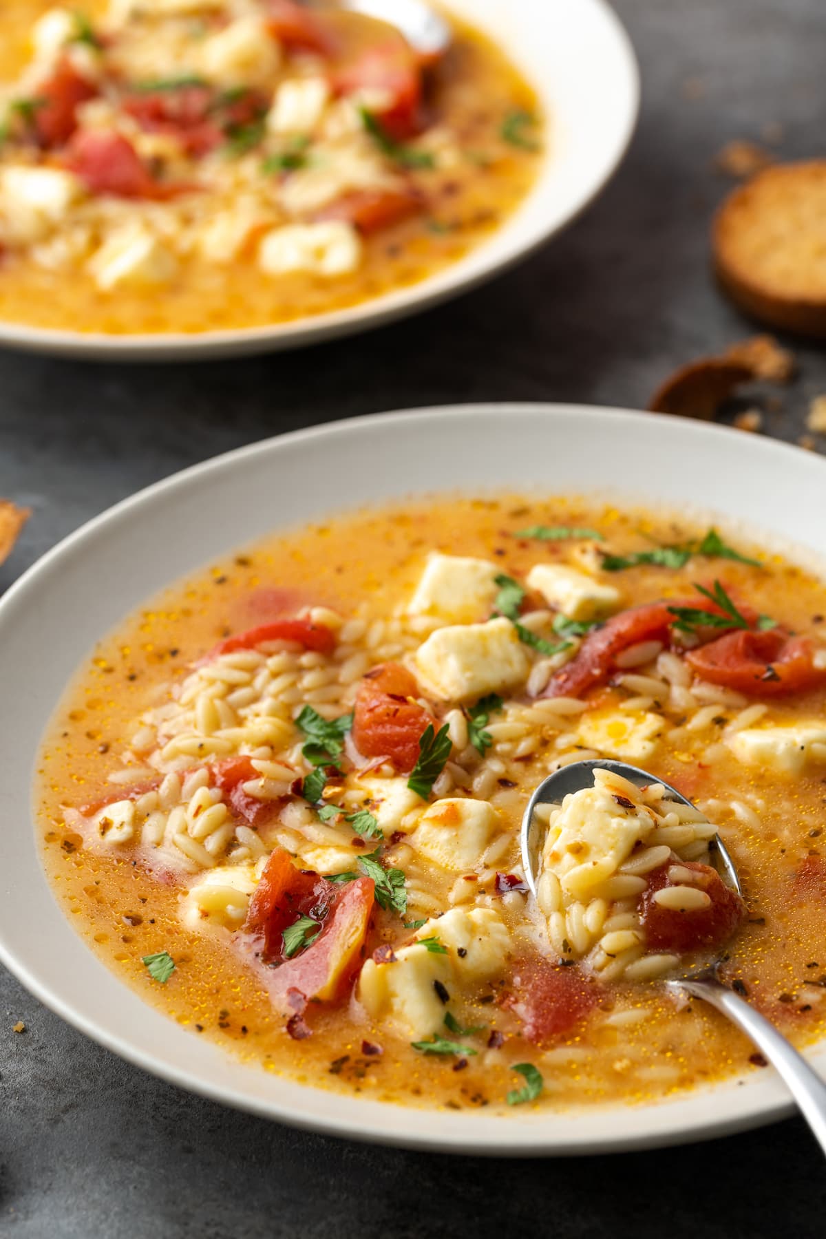 A bowl and spoon of Greek tomato feta soup, another bowl of soup in the background.