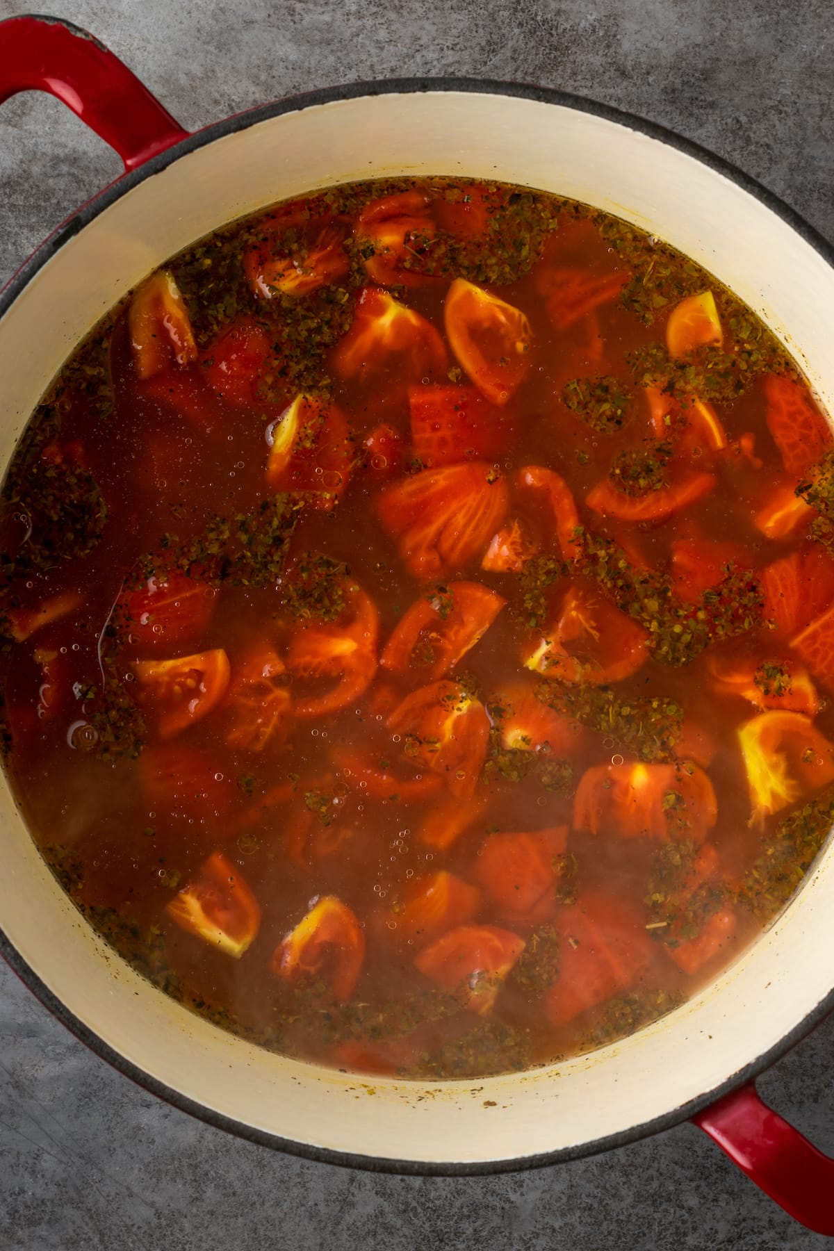 Tomatoes added to a large pot of simmering broth.
