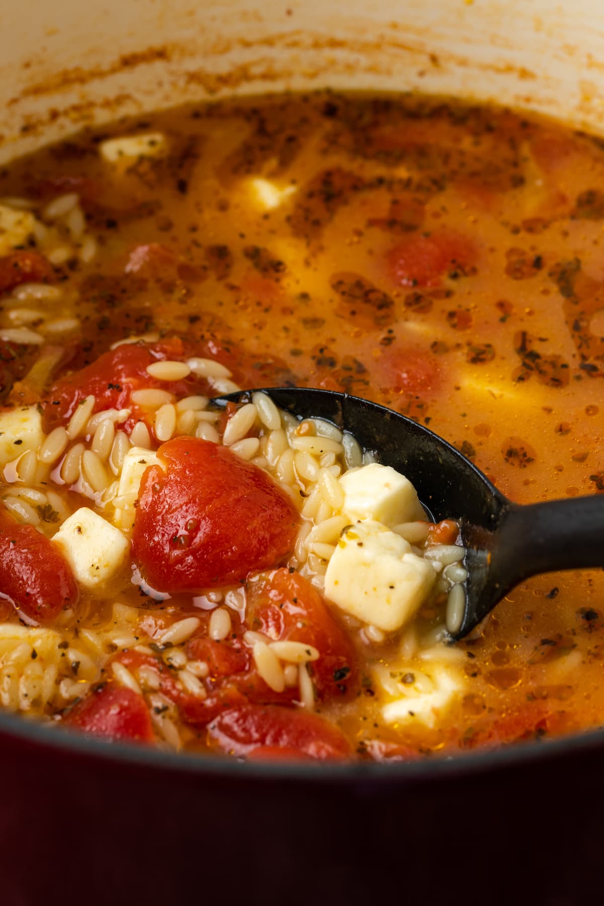 Un cucharón levantando sopa de tomate feta y orzo de una olla grande.