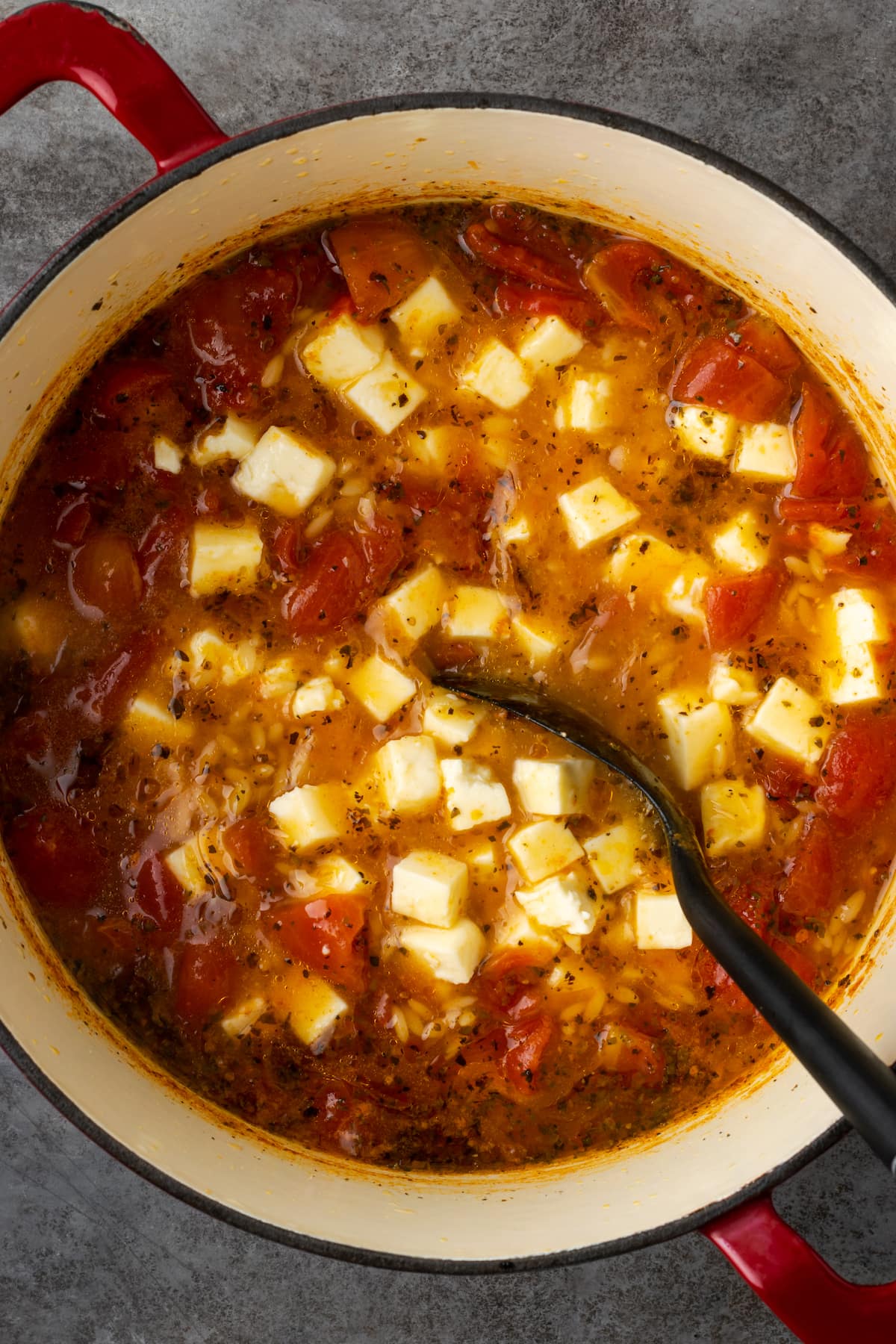 Greek tomato feta soup with a serving spoon in a large pot.