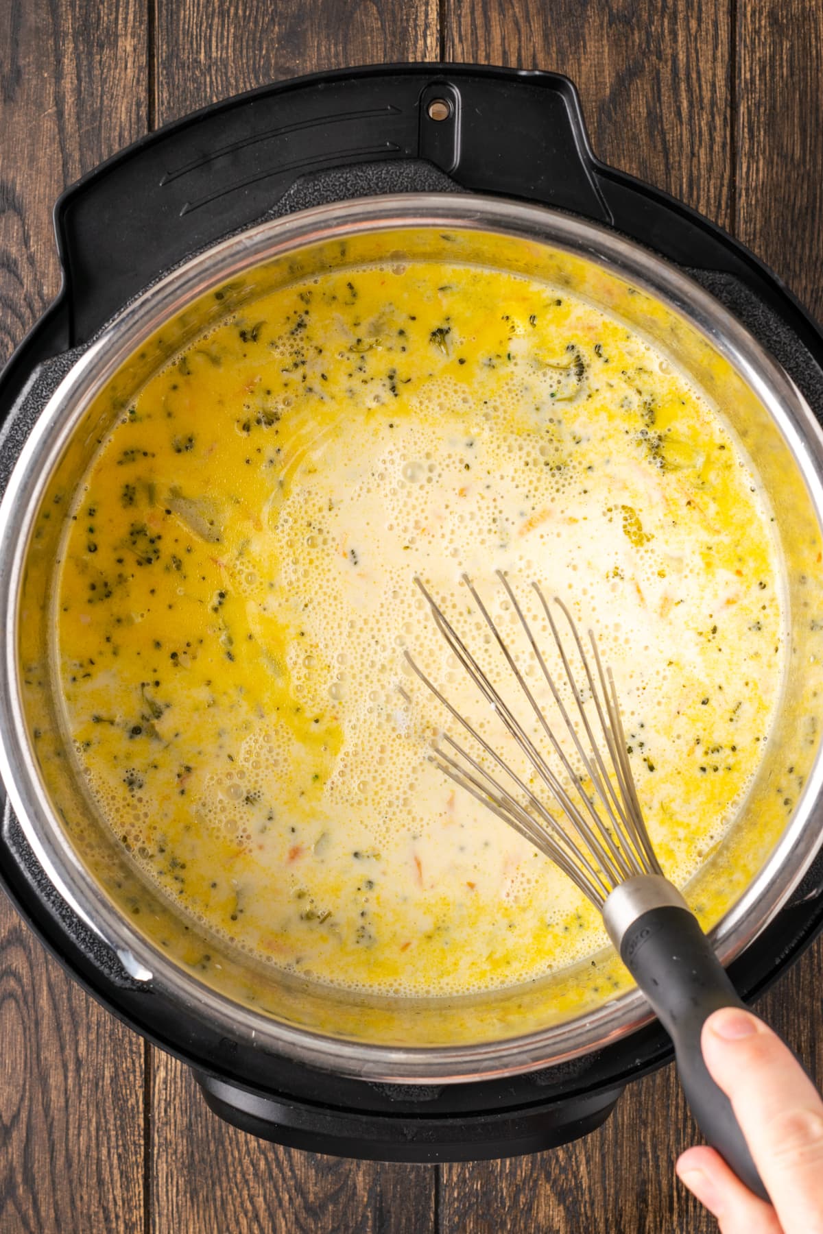 A whisk is used to stir broccoli cheddar soup inside the instant pot.