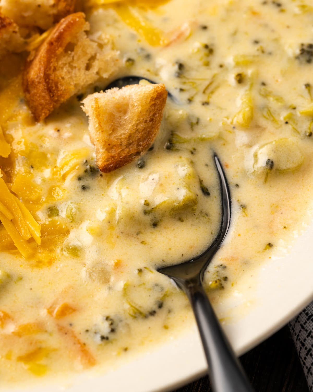 Close up of a bowl of instant pot broccoli cheddar soup topped with croutons with a spoon.