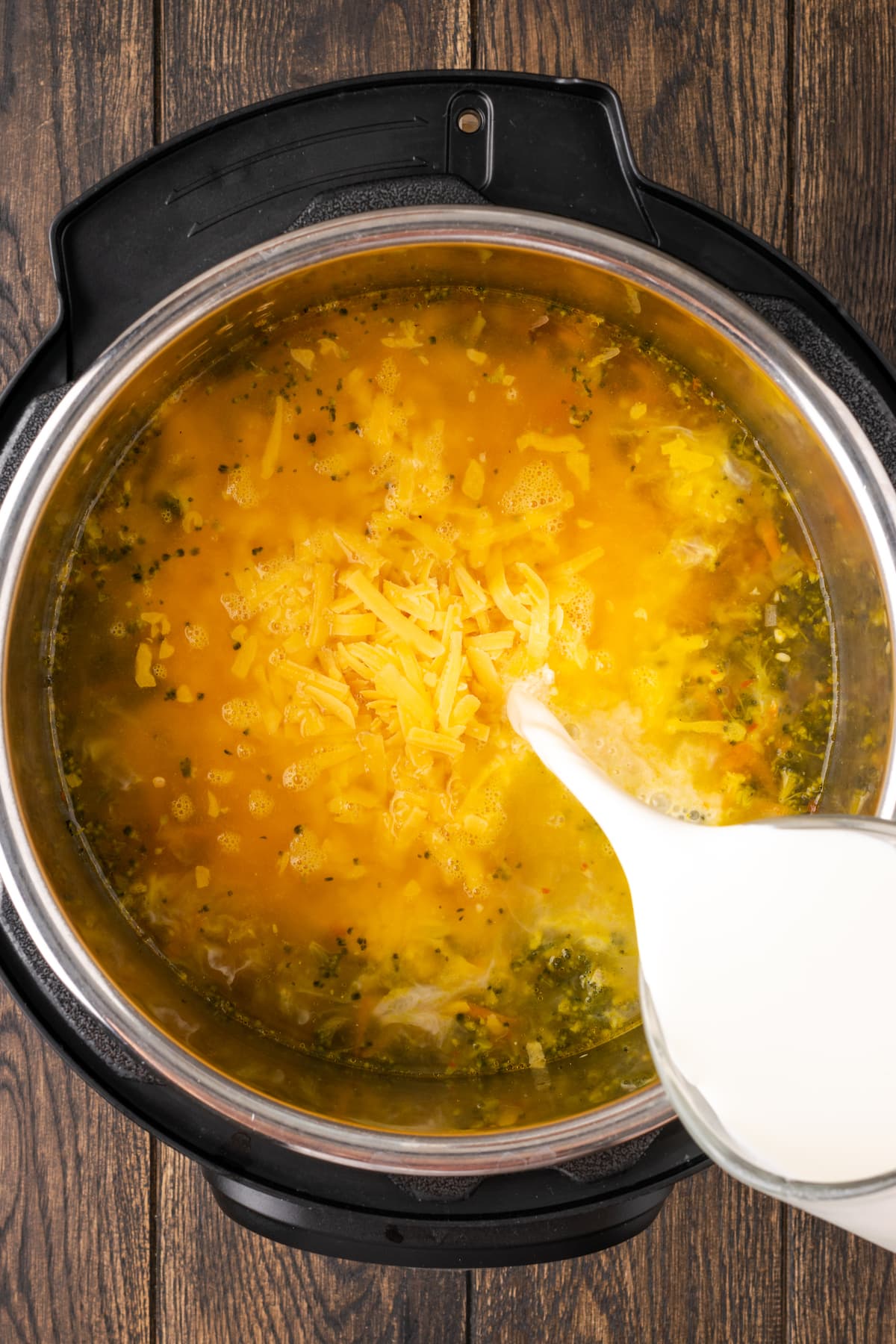 Half-and-half is poured into the instant pot with the other ingredients for broccoli cheddar soup.