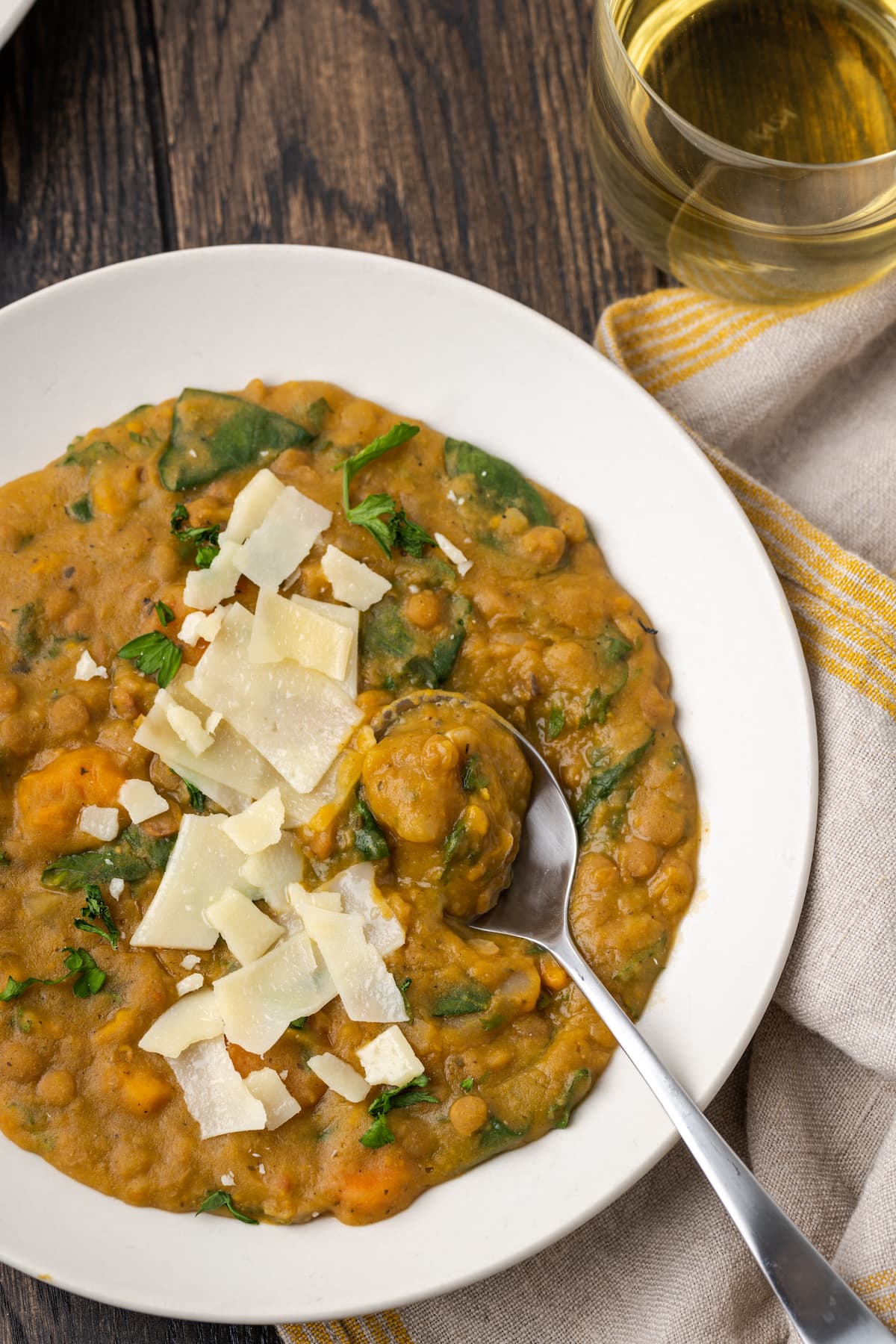 Overhead view of a bowl of lentil soup topped with shaved parmesan cheese, with a spoon.