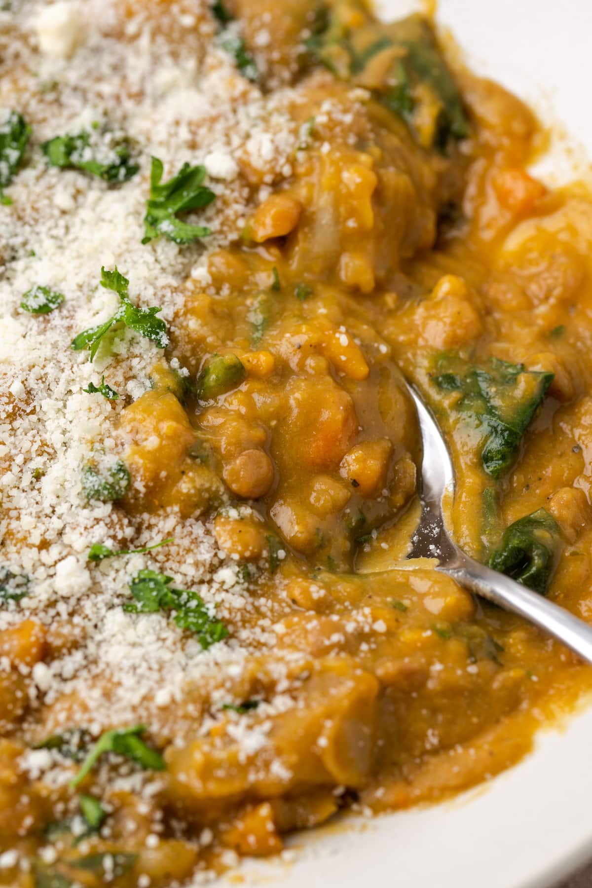 Close up view of a bowl of lentil soup topped with grated parmesan cheese, with a spoon.