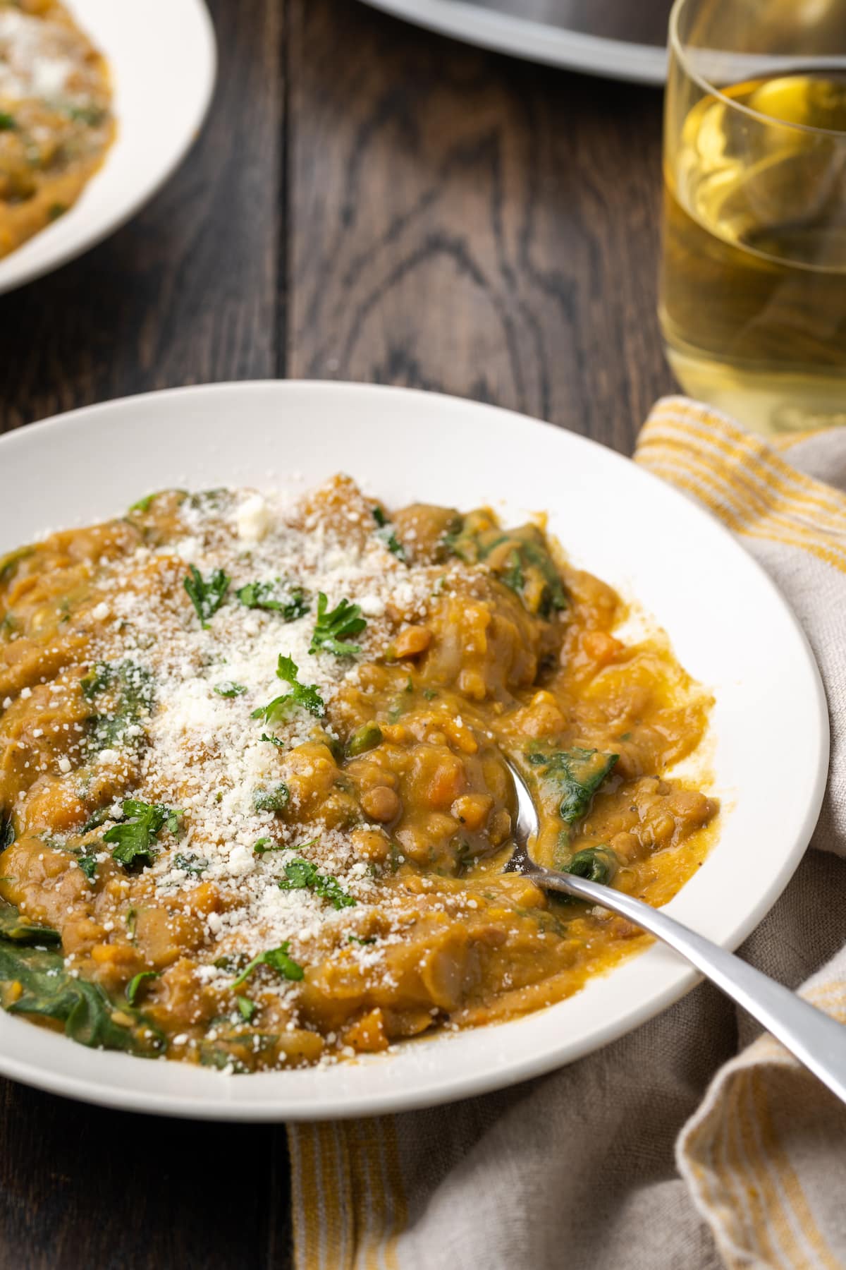 A bowl of lentil soup topped with grated parmesan cheese, with a spoon.