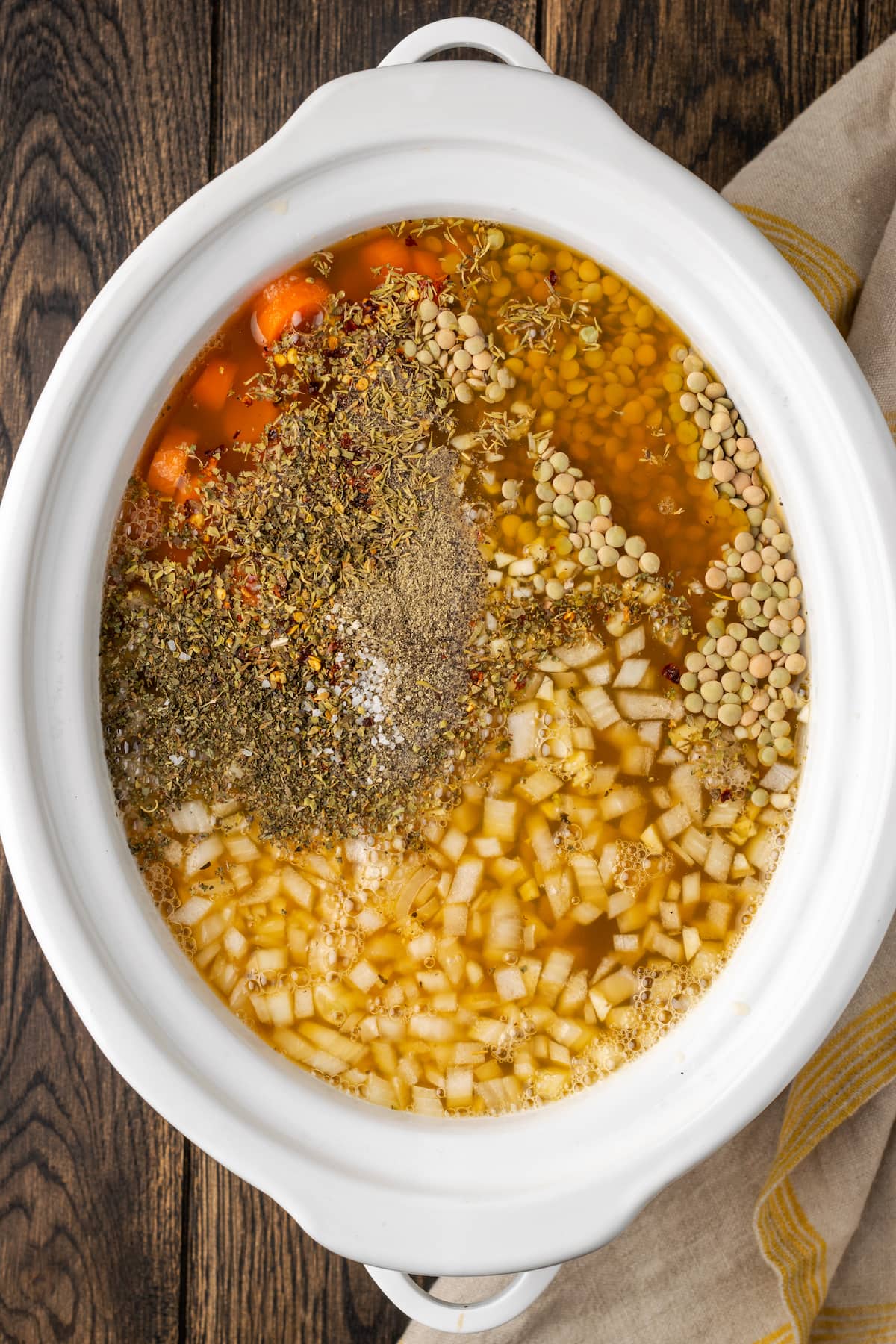 Ingredients for lentil soup assembled in the bowl of a crock pot.