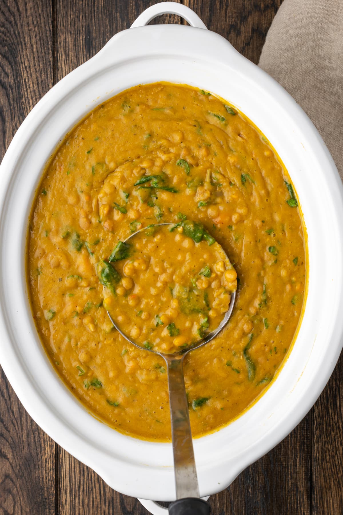 A ladle scoops a serving of lentil soup from a slow cooker.