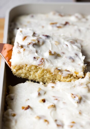 pulling a piece of white sheet cake from the pan with a spatula