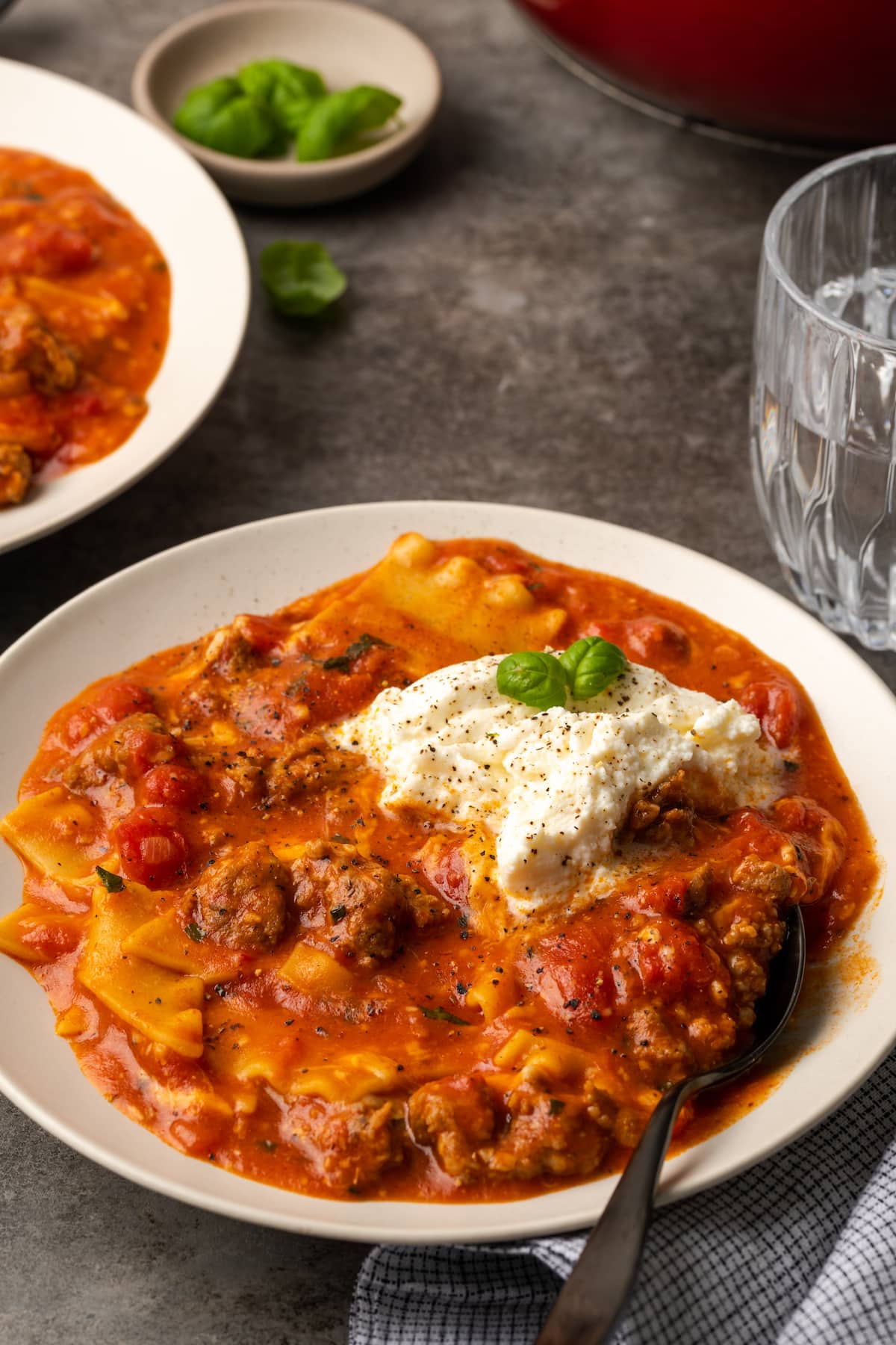 A bowl of lasagna soup topped with ricotta cheese and basil leaves.