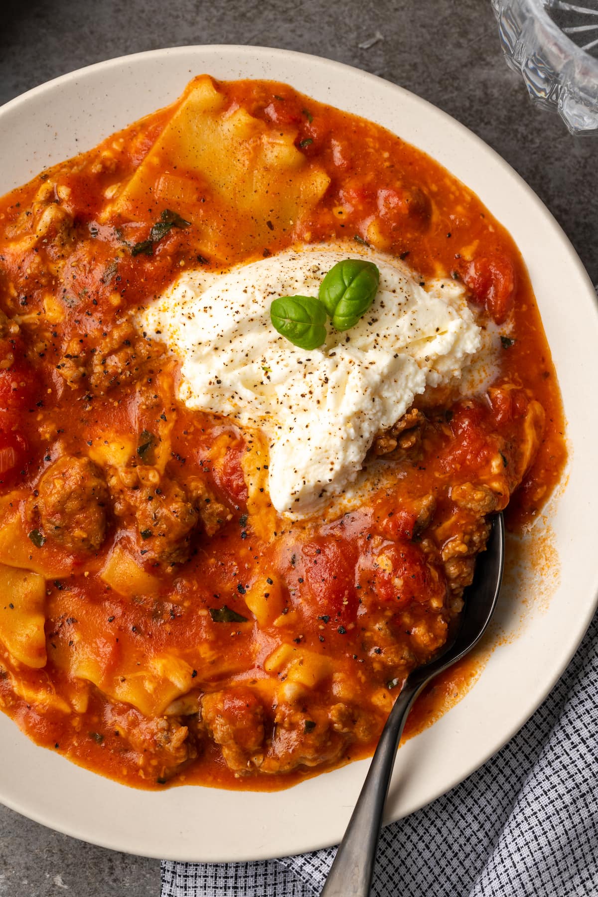 Overhead view of a bowl of lasagna soup topped with ricotta cheese and basil leaves.