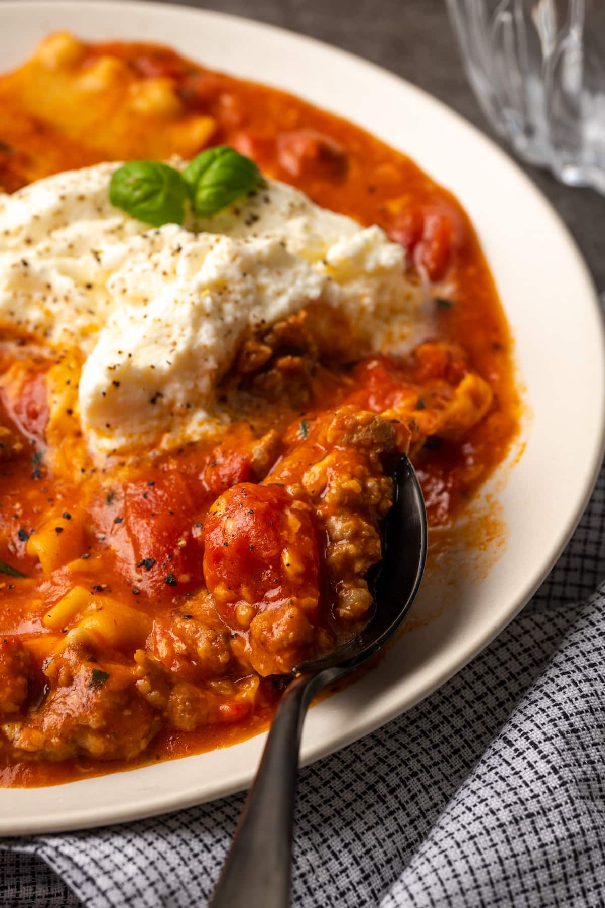 A bowl of lasagna soup topped with ricotta cheese and basil leaves.