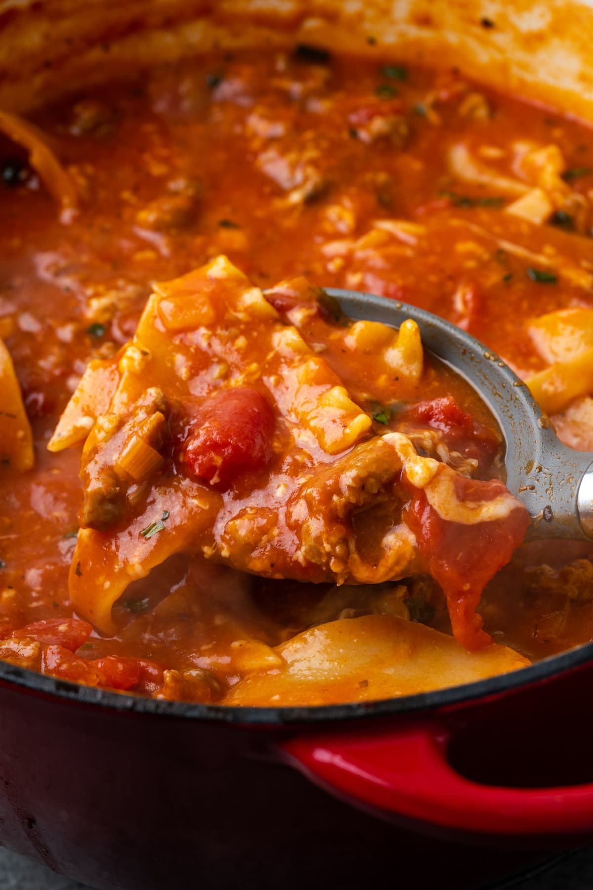 A spoon scooping lasagna soup from a pot.