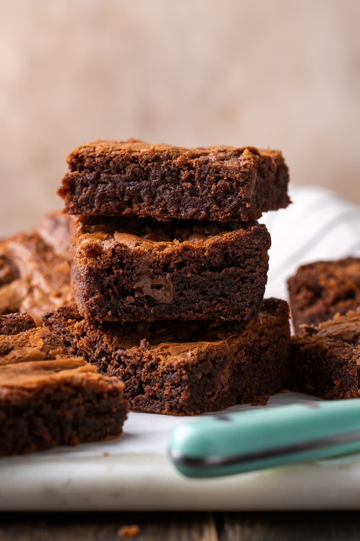 Three Nutella brownies are stacked on a cutting board and surrounded by more brownies.