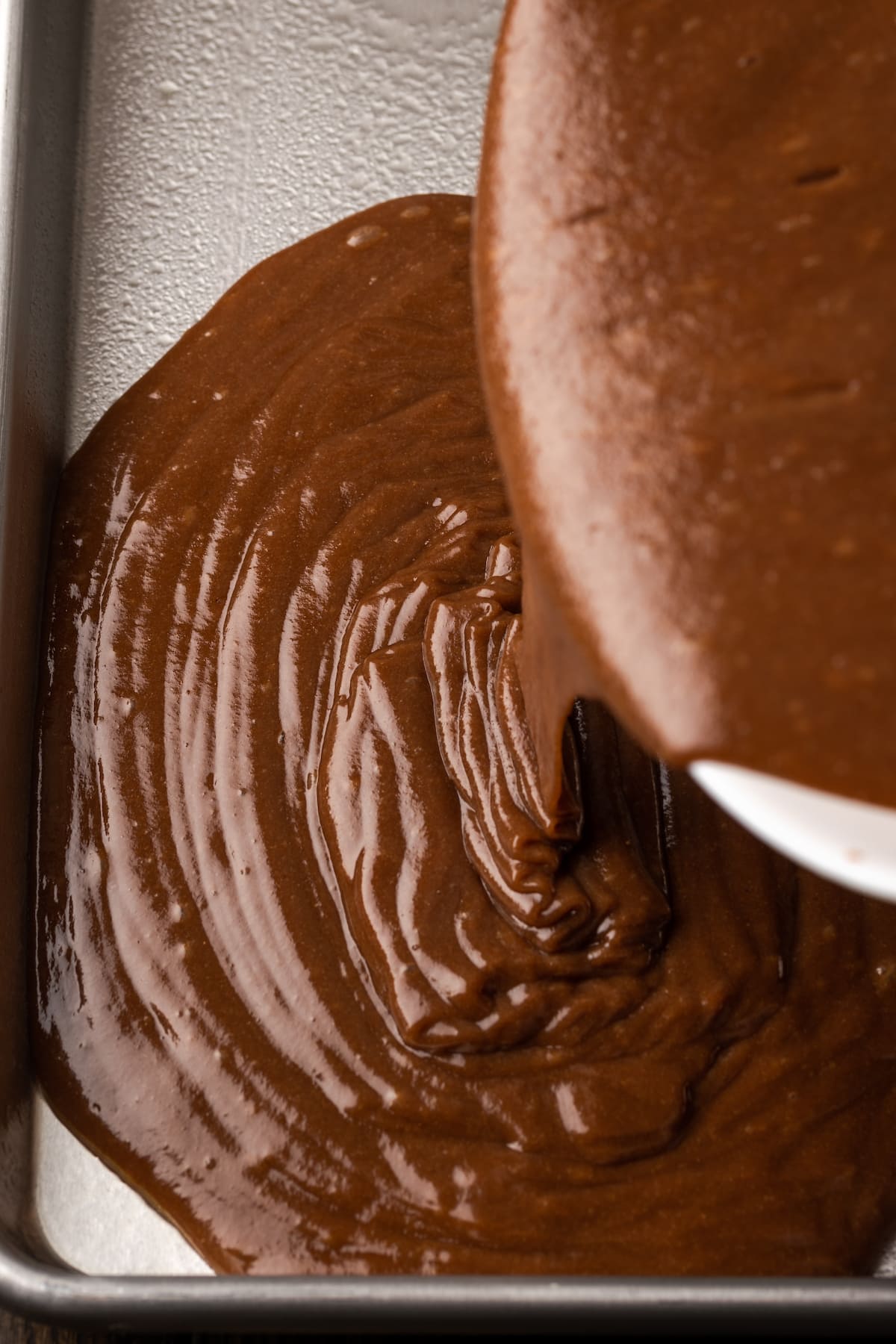 Chocolate cake batter is poured into a sheet pan.