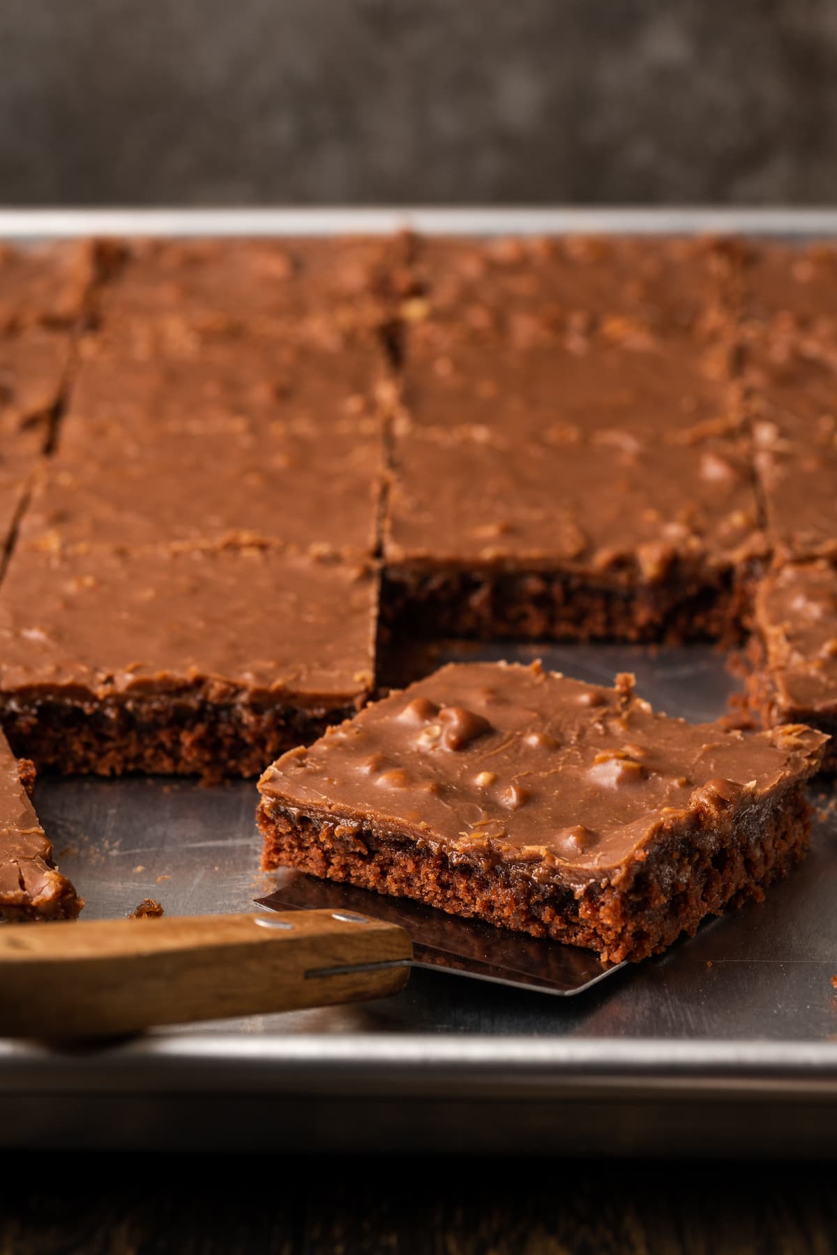 A slice of Texas sheet cake is lifted from a sheet pan with a spatula.