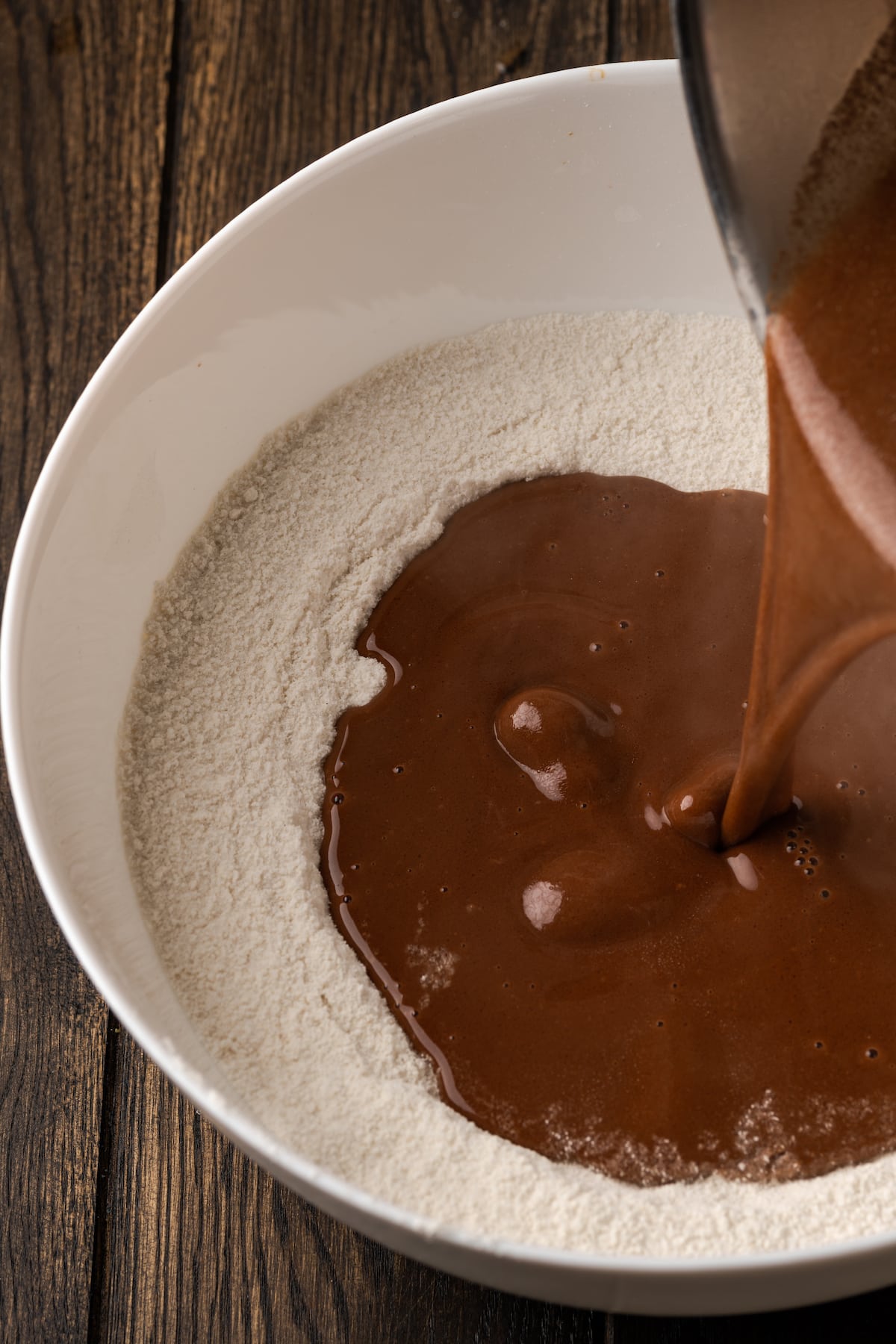 Hot butter mixed with cocoa is poured into a bowl of dry cake batter ingredients.