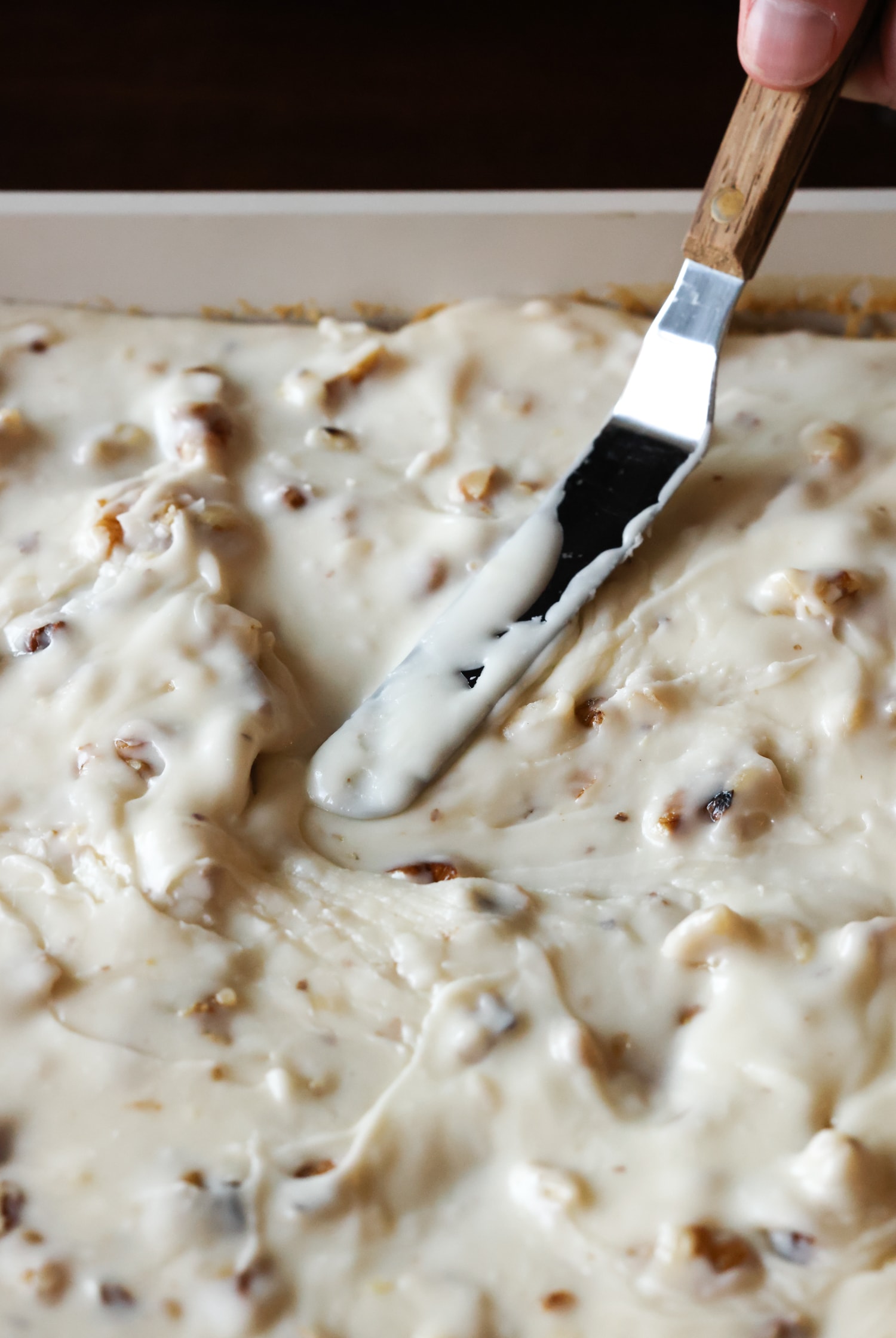 spreading walnut icing onto a cake with an offset spatula