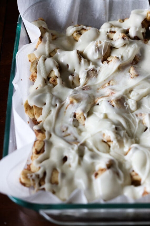 frosting spread on raw cinnamon roll dough in a baking dish